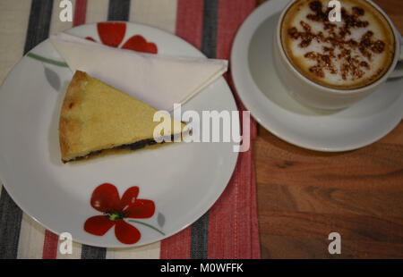 Essen Fotografie mit einem hausgemachten Gebäck und Obst Scheibe der englische Prediger tart auf einem roten und weißen Blumen Teller Tasse Kaffee auf Holz Tisch Stockfoto