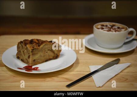 Essen Fotografie aus einer Scheibe hausgemachtes Brot und Butter Pudding auf einem roten und weißen Blumen Muster Platte und eine Tasse Kaffee auf Holz Tisch Hintergrund Stockfoto