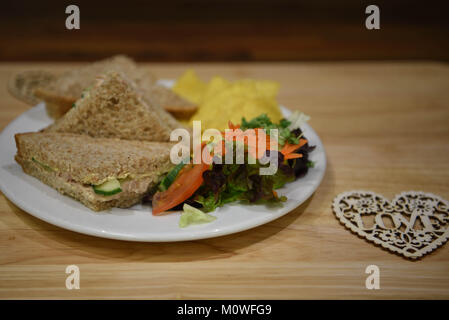 Essen Fotografie eines Mittag essen mit Thunfisch in Dosen und Gurke Sandwiches mit braunem Brot und gesunden Seite Salat auf Holz Hintergrund gemacht Stockfoto