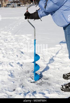 Eine Person bohren ein Loch in das Eis eines zugefrorenen See mit einem Eis auguer (einer spiralförmigen Schraube Blade). Stockfoto