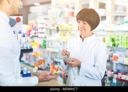 Lächelnd positive Frau Apotheker im weißen Mantel hilft Kunden los im Drug Store zu finden Stockfoto