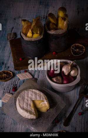 Vertikale Foto von Gegrilltem geschmolzener Camembert. Hot Käse wird auf Papier Blatt mit Schüssel voll mit Zwiebeln und Knoblauch gebraten Kartoffel Streifen in Dosen und d Stockfoto