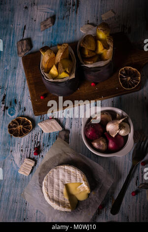 Vertikale Foto von Gegrilltem geschmolzener Camembert. Hot Käse wird auf Papier Blatt mit Schüssel voll mit Zwiebeln und Knoblauch gebraten Kartoffel Streifen in Dosen und d Stockfoto