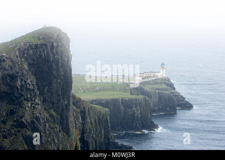 Wanderer auf einer Klippe beobachten Neist Point Leuchtturm im Nebel auf die Isle of Skye, Innere Hebriden, Scottish Highlands, Schottland, UK Stockfoto