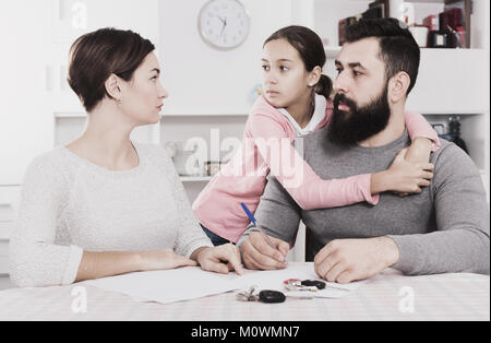 Ernsthafte junge Vater und Mutter Unterzeichnung Scheidung, während ihre Tochter zu Hause Stockfoto