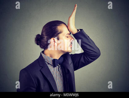 Junge eleganten Mann slapping Stirn mit dummen Fehler, umgekippt, während auf Grau posieren. Stockfoto