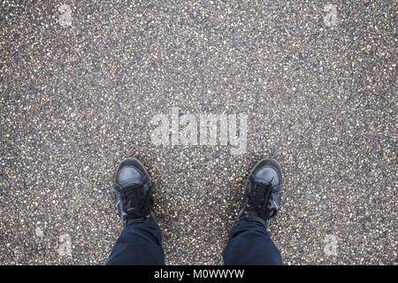 Männliche Füße in Blue Jeans und schwarzem Leder Schuhe stehen auf der Straße Asphalt Stockfoto