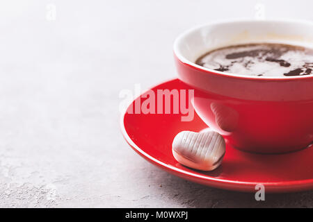 Rot Tasse Kaffee und Schokolade Bonbons in Form eines Herzens über grauer Hintergrund schliessen. Valentinstag Konzept. Stockfoto