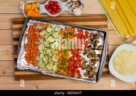 Frische Zutaten bereit Gemüselasagne mit getrockneten Pasta vorzubereiten, gewürfelte Gemüse fein säuberlich auf ein Fach und geriebenen Käse in einem Overhead vie angeordnet Stockfoto