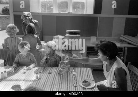 Village Primary School 1970s England. Schulkinder sitzen zusammen mit einem Mitarbeiter an einem Tisch und essen zu Mittag. Schuldame. Cheveley Cambridgeshire 1978 UK HOMER SYKES Stockfoto