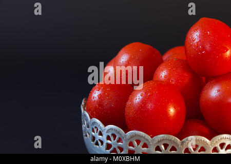 Große rote reife Tomaten mit Tropfen von Wasser in einer Metallschüssel auf schwarzem Hintergrund closeup Stockfoto