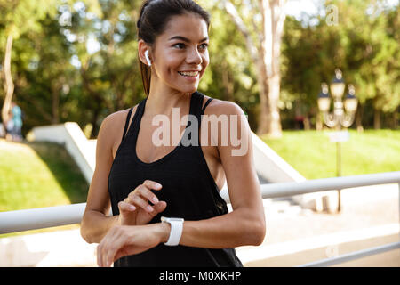 Porträt eines lächelnden fitness Frau in Kopfhörer Ihr smart Watch im Freien prüfen Stockfoto