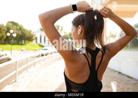 Rückansicht eines jungen Fitness Mädchen der Ohrhörer zur Festsetzung ihr Haar beim Stehen im Freien Stockfoto