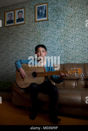 Nordkoreanische Junge spielt Gitarre vor der offiziellen Portraits der liebe Führer an der Wand, auf dem nördlichen Provinzen Provinz, Jung Pyong Ri, Nordkorea Stockfoto