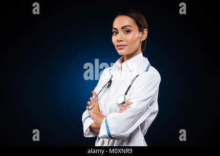 Junge zuversichtlich Dame Arzt in medizinischen Kleid suchen Kamera und halten die Hände gefaltet Stockfoto
