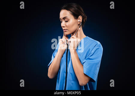 Ernsthafte zuversichtlich, Frau Doktor in der blauen Uniform hören Stethoskop über Schwarz isoliert Stockfoto