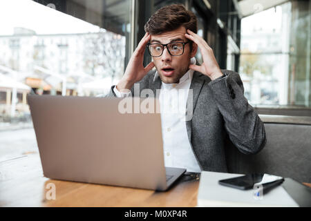 Besorgt verwirrt business Mann in Brillen saßen am Tisch im Cafe halten Kopf und Blick auf Laptop Stockfoto