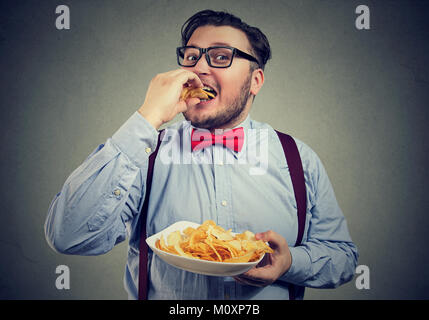 Junge mollig Mann Halteplatte und verschlingende knusprige Kartoffelchips. Stockfoto