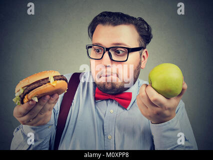 Mollig Mann in Brillen craving leckere Burger statt grün Apple verwirrt. Stockfoto