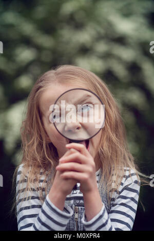 Kind ziehen dumme Gesicht hinter einer Lupe Stockfoto