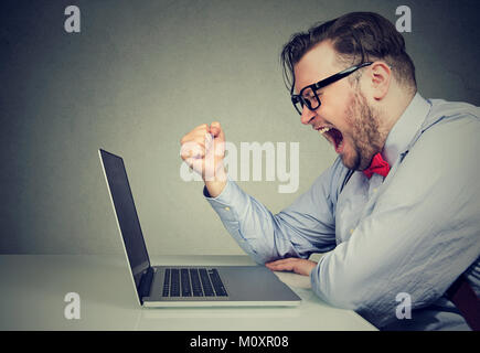 Seitenansicht des Dicklichen jungen Mann in formellen Schreien in der Frustration während der Arbeit mit dem Laptop. Stockfoto