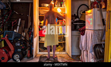 Ein bachelor Mann nur ein Tuch tragen, in der Garage auf der Suche nach Etwas in einem Schrank. Stockfoto