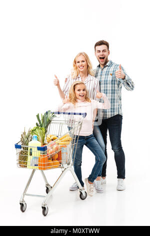 In voller Länge Porträt einer glücklichen Familie mit einem Einkaufswagen voller Lebensmittel und zeigt den Daumen oben-Geste auf weißem Hintergrund Stockfoto