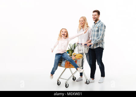 In voller Länge Porträt einer glücklichen Familie wandern mit einem Einkaufswagen voller Lebensmittel auf weißem Hintergrund, kleines Mädchen im Einkaufswagen sitzen Stockfoto