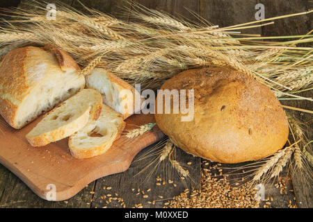 Ganze und geschnittenes Brot mit Ohren und Weizen Korn auf Holz- Hintergrund Stockfoto