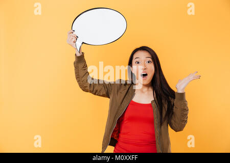 Portrait einer jungen überrascht asiatischen Mädchen, dass leere Sprechblase über Gelb Hintergrund isoliert Stockfoto