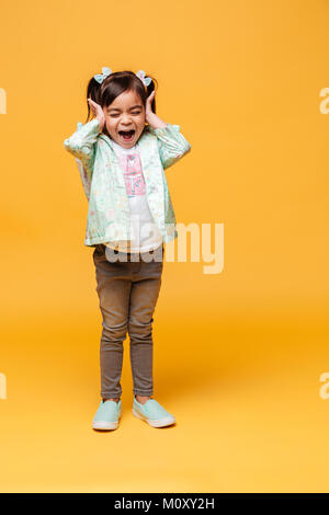 Bild von schreienden emotionale kleine Mädchen Kind stehend über gelben Hintergrund isoliert. Stockfoto