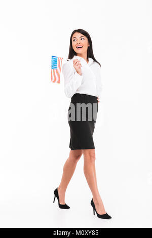 In voller Länge Porträt einer fröhlichen asiatischen Geschäftsfrau, die amerikanische Flagge beim Gehen und entfernten Blick auf weißem Hintergrund Stockfoto