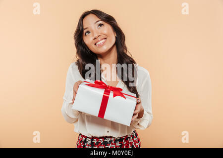 Porträt eines hübschen asiatischen Frau mit Geschenkbox und die Suche nach isolierten über beigen Hintergrund Stockfoto