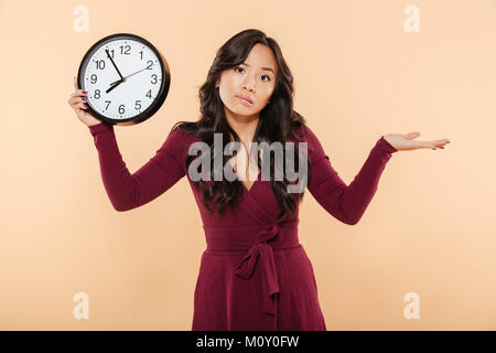 Süße brünette Frau mit lockigen langen Haare, die Uhr zeigt fast 8 zu spät oder fehlt etwas, Kotzte Hand über Pfirsich Hintergrund Stockfoto