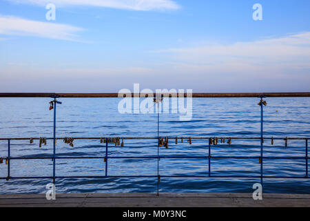 Rusty Vorhängeschlösser Verschlüsse auf geschälte Geländer. Tradition für ein paar in der Liebe. Blauer Himmel und Meer Kulisse. Stockfoto