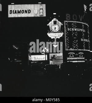 1960, historisches Bild des berühmten Neonreklamen und Werbetafeln beleuchtet die Nacht am Piccadilly Circus Kreisverkehr in Londons geschäftigen West End, London, England, UK. Stockfoto