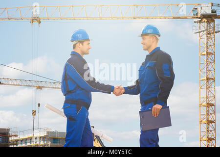 Die Bauarbeiter in Schutzhelmen und blauen Uniform die Hände schütteln Stockfoto