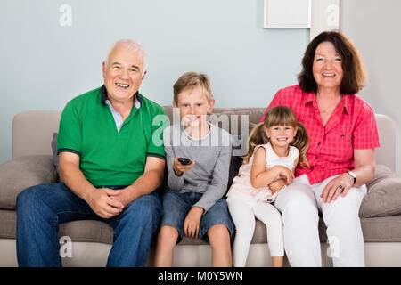 Glückliche Großeltern mit Enkeln Sitzen auf der Couch im Wohnzimmer Fernsehen Stockfoto