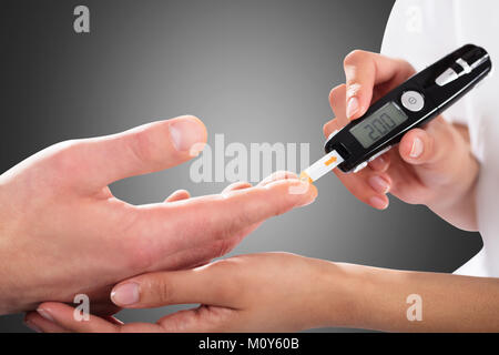 Nahaufnahme einer Person Kontrolle der Blutzuckerspiegel durch Glucometer auf grauem Hintergrund Stockfoto