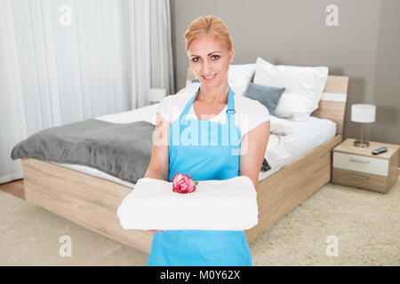 Portrait von lächelnden Jungen Hotel Zimmermädchen Holding Stapel frische saubere Handtücher im Zimmer Stockfoto