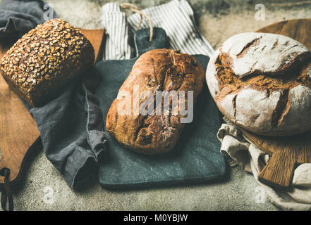 Verschiedene Brot Auswahl. Roggen, Weizen und multigrain Rustikales Brot Brote auf Küche Handtücher und Holzbretter über grauer Beton Stein Hintergrund Stockfoto