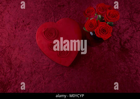 Valentine Hintergrund, rote Leathered Herz geformten Süßigkeiten, mit frischen Rote Rose Bouquet auf rotem Hintergrund, Stockfoto
