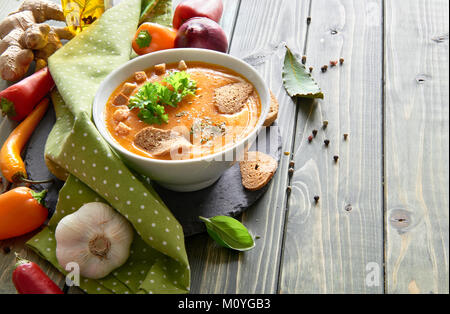 Würzige Gemüsesuppe mit gebratenen Paprika, Tomaten, Karotten, Paprika, rote Zwiebel, Knoblauch und Ingwer in Keramik Schüssel auf den Holztisch. Die Suppe ist Stockfoto