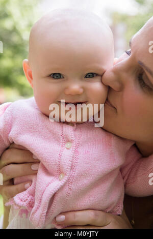 Portrait der kaukasischen Mutter küssen Wange von baby Tochter Stockfoto