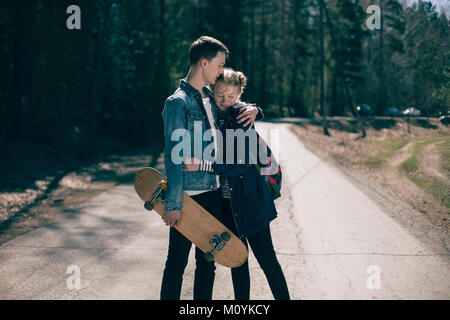 Kaukasische Paar mit Skateboard umarmen im Straßenverkehr Stockfoto