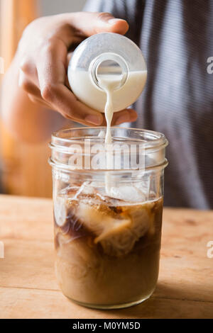 Afrikanische amerikanische Frau gießen Milch in jar von Kaffee Stockfoto