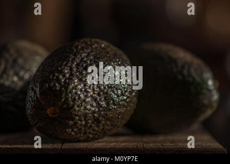 Nahaufnahme von mehreren Avocados in Moody natürliche Beleuchtung auf einem Holzbrett Stockfoto