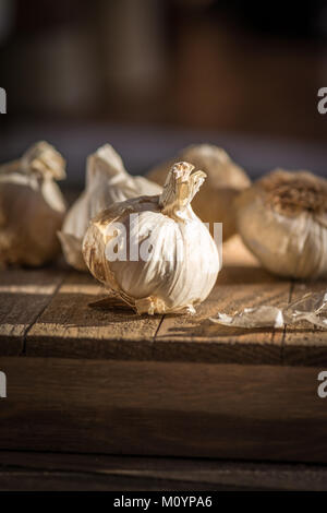 Einige Leiter von frischem Knoblauch auf einem Holzbrett mit dunklem Hintergrund bei natürlichem Licht Stockfoto