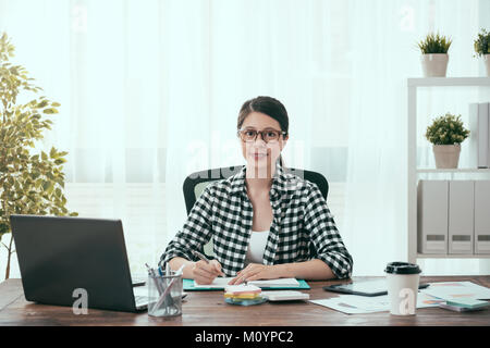 Ziemlich sicher weibliche business Worker zu Hause arbeiten und sitzen am Arbeitsplatz zimmer Verarbeitung Unternehmen arbeiten bei der Kamera schaut. Stockfoto