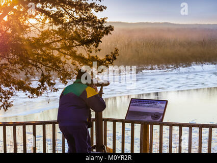 Mann beobachten Eisschollen auf dem Missouri River von einem Holzdeck durch ein Teleskop; interpretierende Zeichen von der Missouri Wildlife Refuge auf der rechten Seite Stockfoto